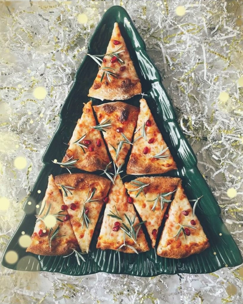 Pizza slices arranged to look like a Christmas tree on a pine tree-shaped tray, decorated with sprigs of rosemary and dried cranberries.