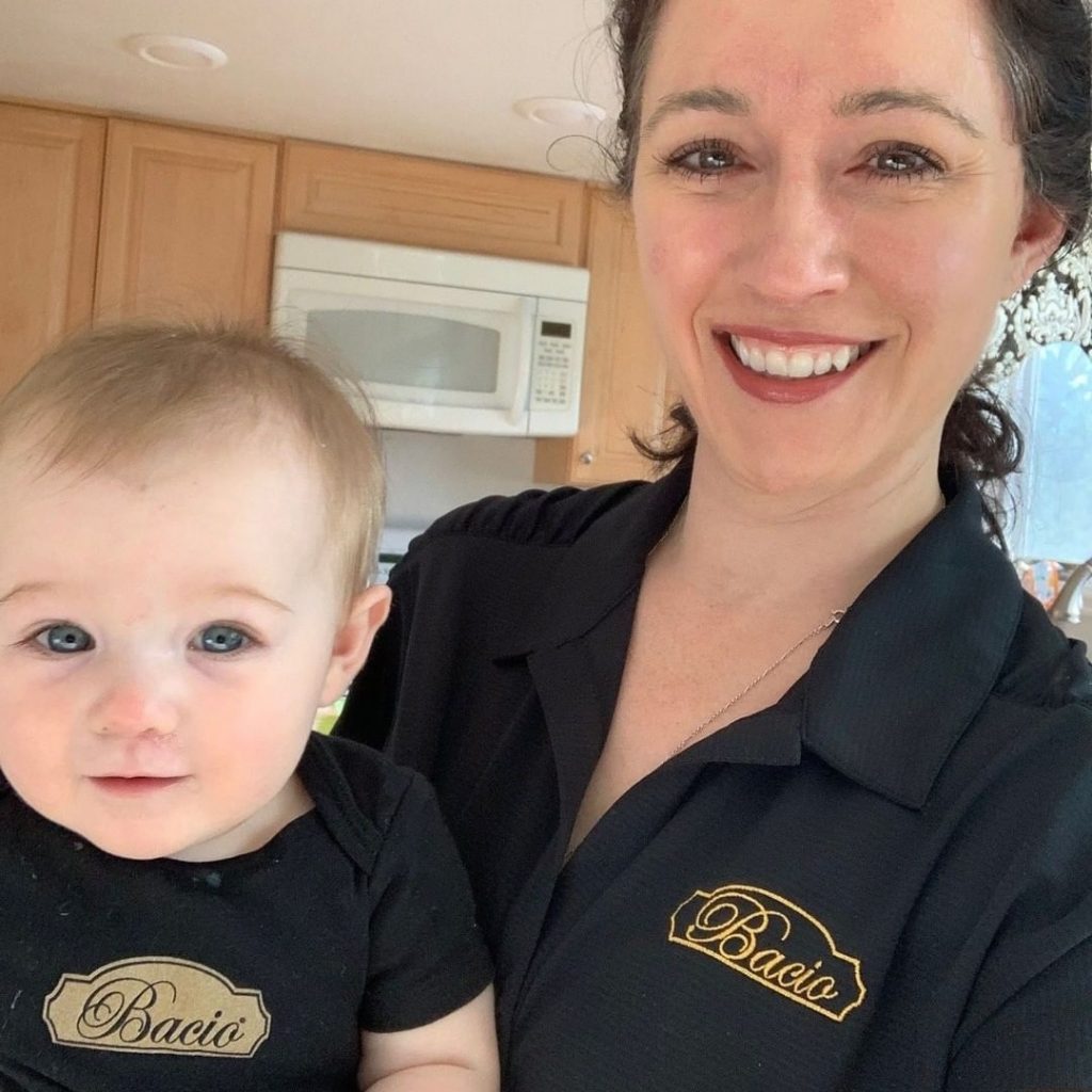 team member Bridget holding her baby. Both are wearing Bacio-branded shirts.