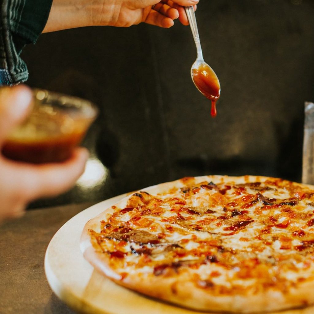 Spooning BBQ sauce onto a Texas-style BBQ pizza