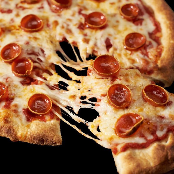 close up of a slice of pepperoni pizza being pulled away from the pizza and the cheese stretching between the two